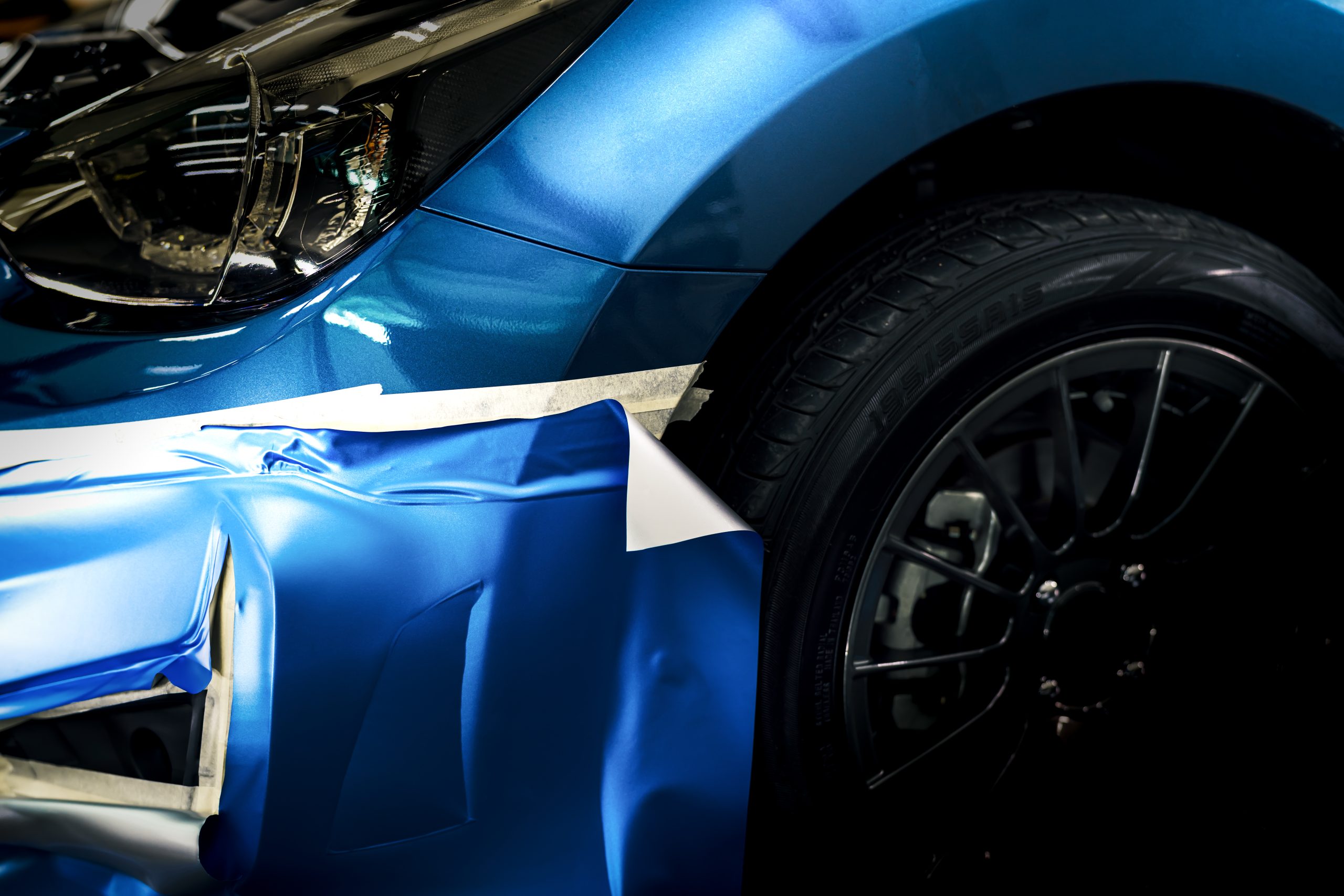 Decals graphics on a blue car show a partially peeled vinyl wrap revealing the original surface underneath