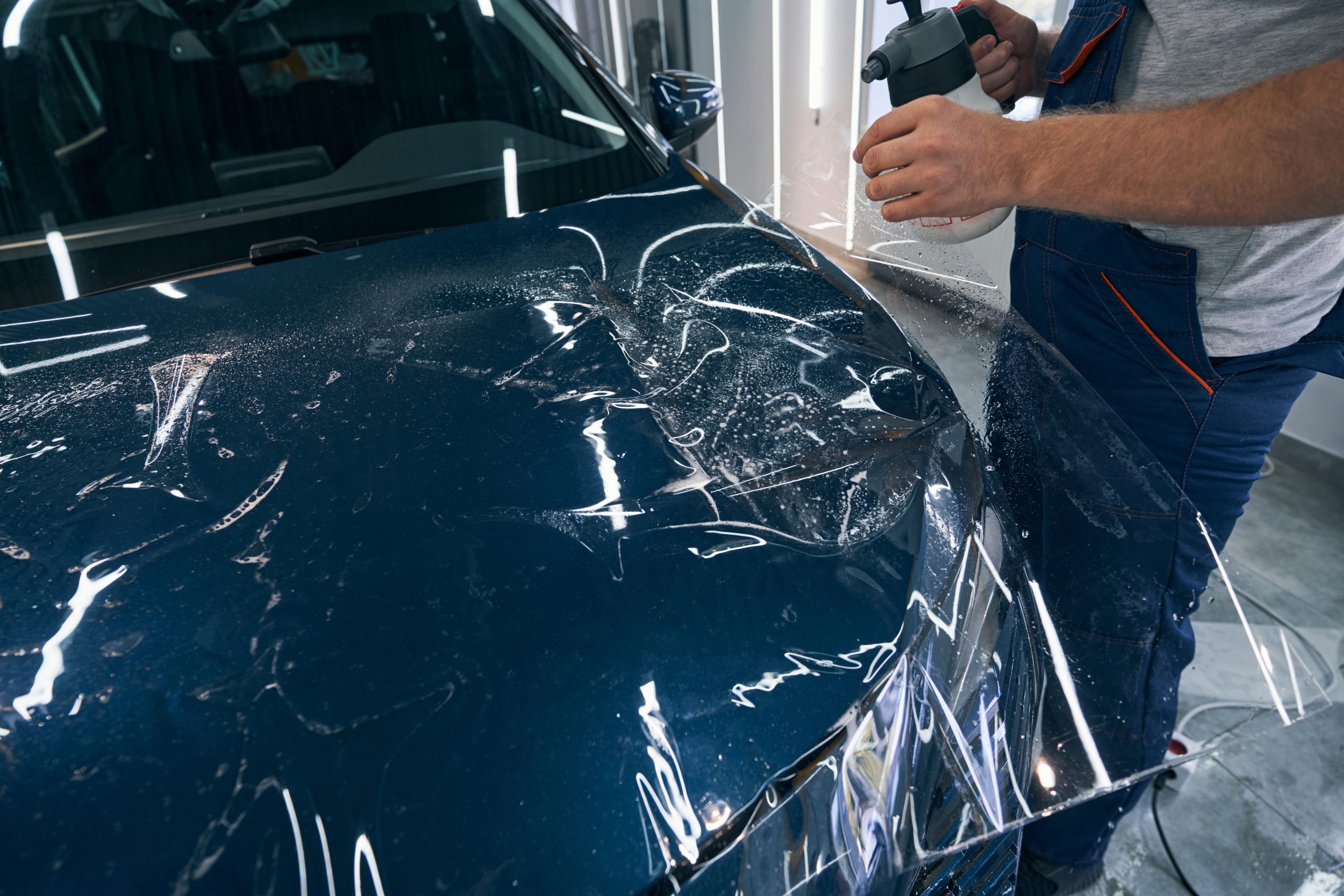 A person applies paint protection film to a shiny blue car's hood