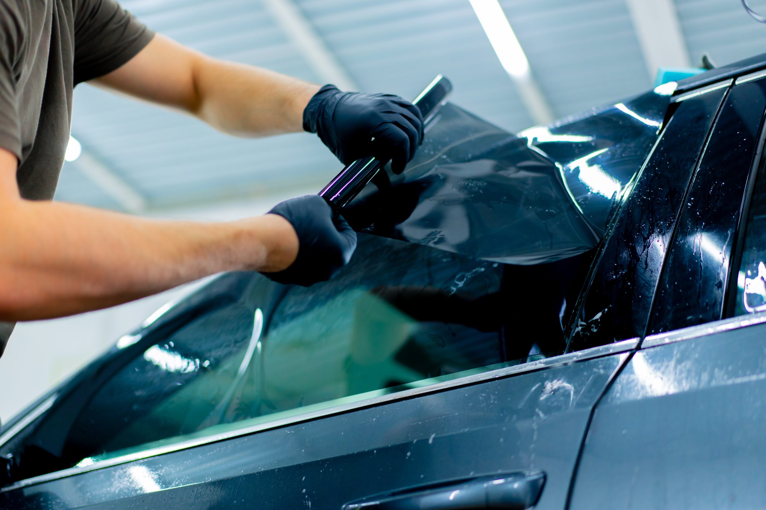 A person applying dark window tinting film to a car's window
